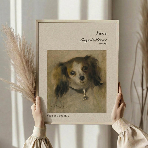 May include: Hands holding a framed reproduction of Renoir's 1870 dog portrait showing a small spaniel-type dog with long ears and collar against cream matting. Person wears cream ruffle-sleeved top, holding dried wheat stems. Soft natural lighting creates neutral, minimalist aesthetic with white curtained background.
