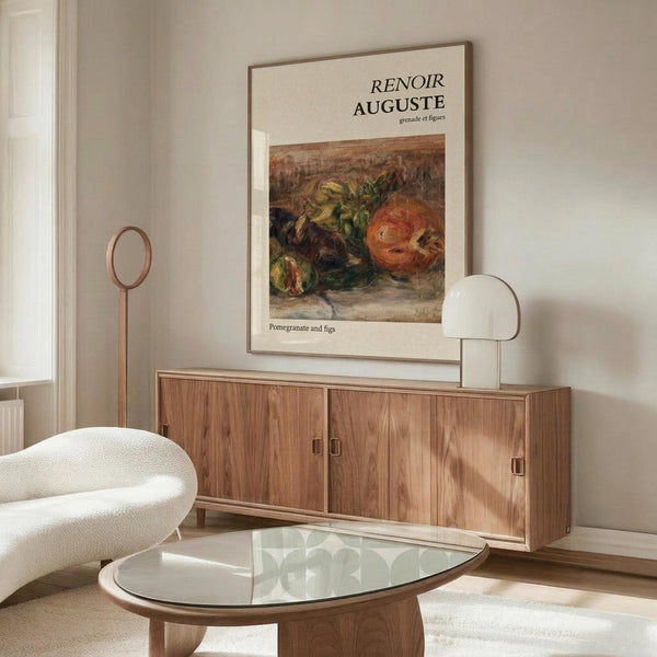 May include: Renoir still life poster showing pomegranates and figs in warm reds, oranges and greens, framed and displayed above a walnut wood credenza in a minimalist living room. White curved chair and glass-top oval coffee table visible. Natural lighting creates soft shadows on cream walls.