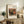 May include: Framed art print featuring a still life painting of pomegranate and figs in warm earthy tones, displayed on a rustic wooden sideboard alongside books, a ceramic vase, and fern plant in a neutral-toned living room setting with cream armchair and throw pillows.