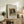 May include: Framed vintage-style dog portrait poster displayed on rustic wooden console table alongside fern plant, ceramic vases, and books. The artwork shows a small spaniel-type dog with long ears and collar in muted brown tones. Light wood frame with white matting against cream wall in cozy living room setting with upholstered chair visible.
