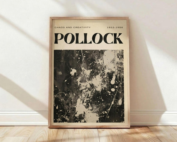 May include: Framed poster print leaning against white wall on light wood floor. Cream-colored poster features large black "POLLOCK" text and abstract black paint splatters on white background. Top text reads "CHAOS AND CREATIVITY 1912-1956" in small capitals. Natural wood frame with light stain. Soft window light creates diagonal shadows across white textured wall and warm wood grain flooring.