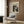 May include: Beige framed art print featuring Jackson Pollock's black and white abstract splatter painting with "POLLOCK" and "CHAOS AND CREATIVITY" text, displayed on wood paneled wall above cream upholstered armchair with geometric patterned pillow, beside brass floor lamp and dark round side table with open book