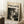 May include: Framed poster with cream background featuring "POLLOCK" in large black letters, "CHAOS AND CREATIVITY 1912-1956" text above, and abstract black paint splatter artwork below. Light wood frame leaning against white wall next to wooden side table with white coffee cup and saucer, beige textured rug visible.