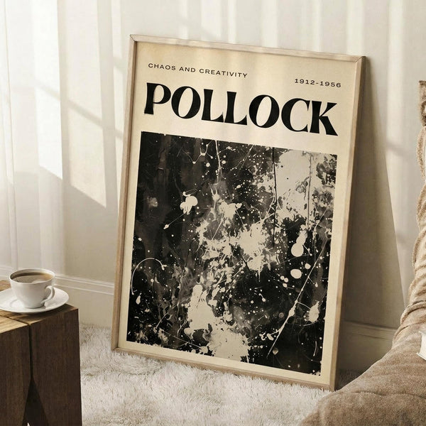 May include: Framed poster with cream background featuring "POLLOCK" in large black letters, "CHAOS AND CREATIVITY 1912-1956" text above, and abstract black paint splatter artwork below. Light wood frame leaning against white wall next to wooden side table with white coffee cup and saucer, beige textured rug visible.