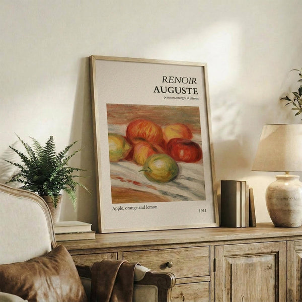 May include: Framed art print featuring Renoir's colorful still life painting of apples, oranges and lemons displayed on rustic wooden sideboard next to fern plant, books, ceramic vase and beige upholstered chair in neutral-toned living room setting