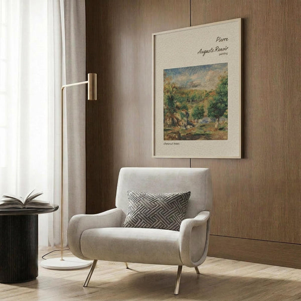 May include: Beige upholstered armchair with geometric patterned throw pillow positioned next to framed Renoir landscape print on wood paneled wall. Brass floor lamp with white circular base stands beside chair. Dark round side table with open book visible on left. Warm neutral tones throughout modern living room setting with natural lighting from window.