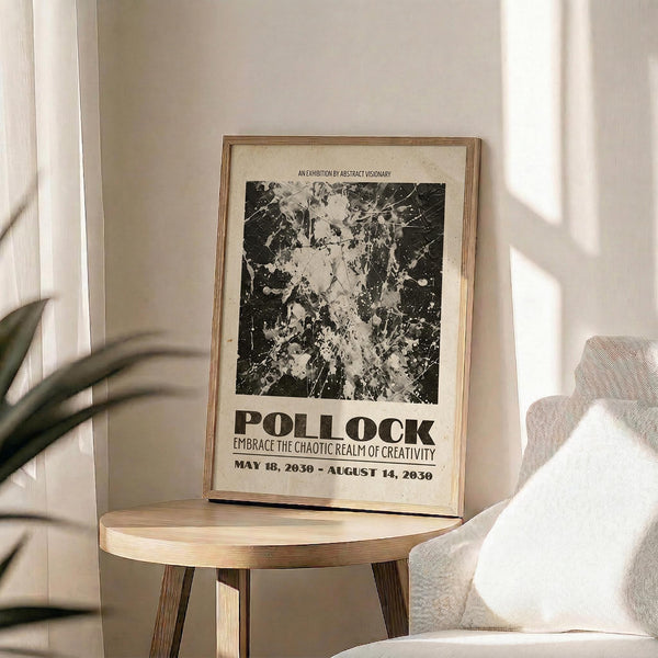May include: Black and white abstract expressionist poster with paint splatters and drips displayed in thin gold frame on round wooden side table. Cream colored wall backdrop with soft natural lighting creating shadows. Beige upholstered chair partially visible on right side, plant leaves in corner. Exhibition-style poster features bold typography and chaotic paint texture artwork reminiscent of mid-century abstract painting style.