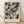 May include: Black and white abstract expressionist artwork in light wood frame, featuring dynamic paint splatters, drips, and gestural brushstrokes across cream background. Text below reads "POLLOCK" and "Expressive Expressionist Movement". Frame leans against white textured wall on light wooden floor with soft natural lighting and shadow patterns.