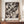 May include: Black and white abstract expressionist artwork with dramatic paint splatters, drips, and gestural brushstrokes displayed in a thin wooden frame on a mid-century modern credenza beside a cream ceramic vase and stacked books in an elegant room with beige walls and classical molding.