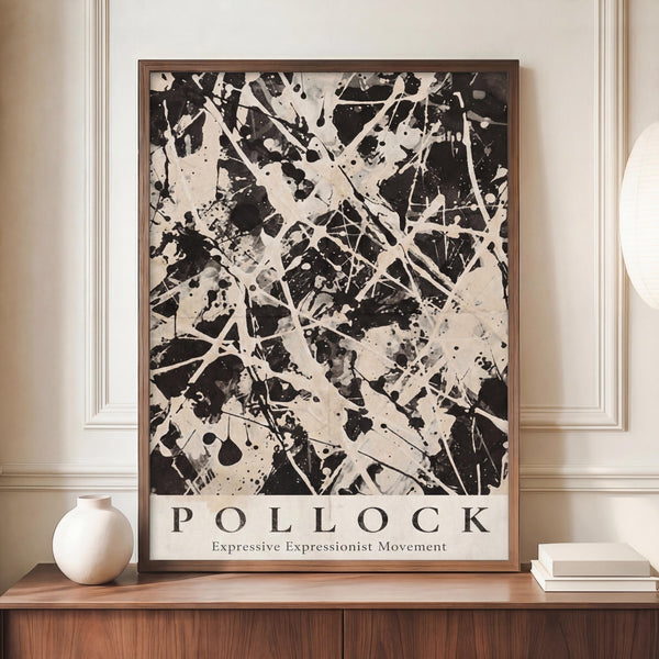 May include: Black and white abstract expressionist artwork with dramatic paint splatters, drips, and gestural brushstrokes displayed in a thin wooden frame on a mid-century modern credenza beside a cream ceramic vase and stacked books in an elegant room with beige walls and classical molding.