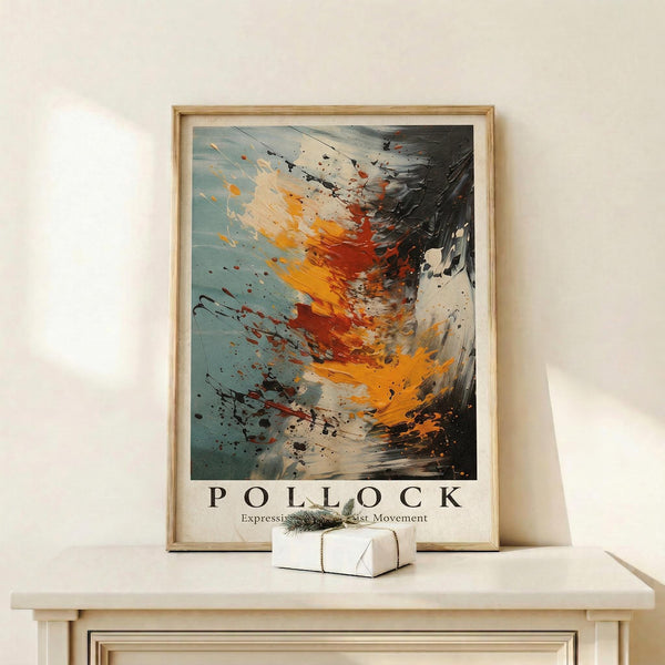 May include: Abstract expressionist artwork in wooden frame leaning against white wall on light wood console table. The painting features dynamic splashes and drips in orange, red, black, white and blue-gray tones creating energetic movement across the canvas. A small white wrapped gift with evergreen sprig sits in front of the framed piece. Soft natural lighting creates gentle shadows on the minimalist white wall backdrop.