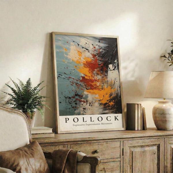 May include: Abstract expressionist art print in light wood frame displaying energetic paint splatters and brushstrokes in orange, red, black, and blue tones against cream background. Poster sits on rustic wooden sideboard next to fern plant, ceramic vase, and stacked books in warmly lit living room with beige armchair.