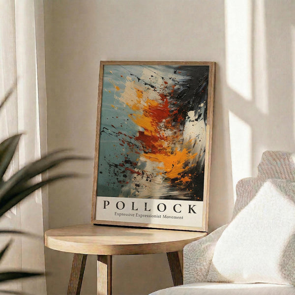 May include: Abstract expressionist artwork poster in wooden frame, featuring dynamic splashes and drips in orange, red, black, and blue against cream background, displayed on round wooden side table next to beige upholstered chair with plant leaves visible, warm natural lighting creating soft shadows on neutral wall.