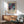 May include: Abstract art poster with cosmic swirls in deep blues, purples, and teals with golden dots and flowing lines, displayed in wooden frame above mid-century modern credenza with table lamp, next to sage green upholstered armchair with wooden arms in sunlit room with white walls and hardwood floors.