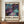 May include: Abstract art poster with swirling cosmic design in deep purples, teals, and blues with golden splashes and dots, displayed in brown frame on wooden sideboard next to white ceramic vase and books. Exhibition-style poster features "POLLOCK" text and "Embrace the Chaotic Realm of Creativity" tagline below flowing, galaxy-like artwork with organic curves and scattered circular elements.
