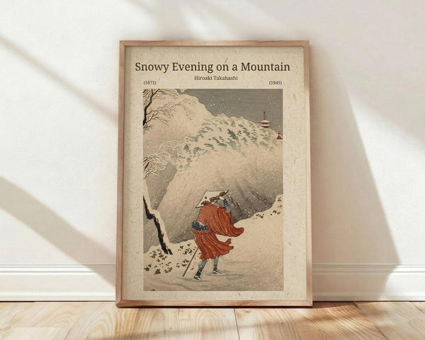 May include: Framed vintage Japanese woodblock print showing a figure in flowing red robes walking through heavy snowfall on a mountain path, with snow-covered peaks and bare trees in muted earth tones. Wooden frame displayed on light wood floors against white wall with natural window lighting casting soft shadows.