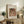 May include: Framed art print of Renoir's impressionist painting featuring a woman with dark hair wearing a pink headscarf, displayed on rustic wooden sideboard alongside books and potted plants including ferns and olive branches in neutral-toned living room setting