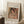 May include: Framed art print of a Renoir painting featuring a woman with dark hair wearing a coral headband and pearl necklace, displayed in a light wood frame against white walls. Scene shows the print leaning on a textured cream rug next to a wooden side table with white coffee cup, creating a cozy interior setting with natural window lighting.