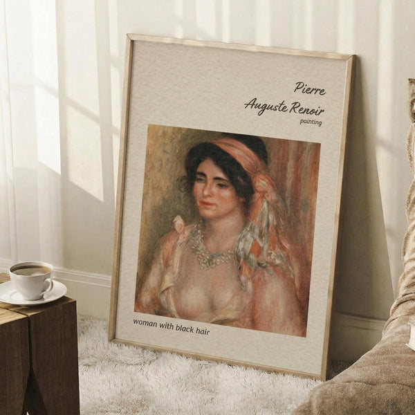 May include: Framed art print of a Renoir painting featuring a woman with dark hair wearing a coral headband and pearl necklace, displayed in a light wood frame against white walls. Scene shows the print leaning on a textured cream rug next to a wooden side table with white coffee cup, creating a cozy interior setting with natural window lighting.