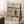 May include: A framed Japanese woodblock print poster leaning against a white wall, showing a snow-covered temple pagoda and figure with umbrella in muted earth tones. The beige wooden frame sits on a white textured rug beside a coffee cup on a wooden block and cream blanket.