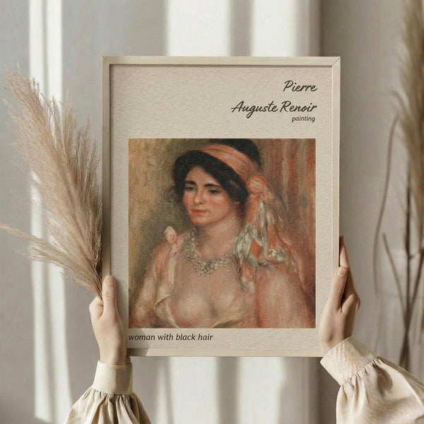 May include: Hands holding a framed reproduction of a Renoir painting showing a woman with dark hair wearing a coral headband and pearl necklace. The artwork is displayed in a light wooden frame against cream-colored fabric with dried wheat stalks visible to the left side.