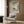 May include: Japanese woodblock print style poster featuring a large sailing ship with multiple masts in coastal waters, displayed in white frame on wood-paneled wall above beige upholstered armchair with geometric patterned pillow, modern brass floor lamp, and dark round side table with open book visible in minimalist room setting