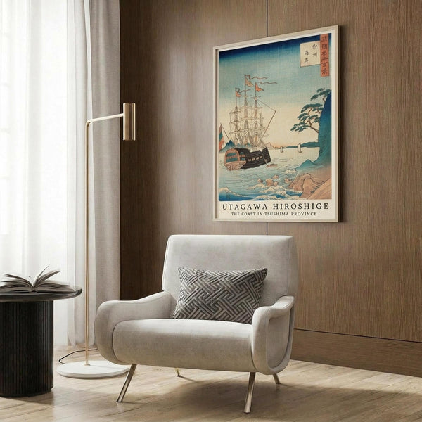 May include: Japanese woodblock print style poster featuring a large sailing ship with multiple masts in coastal waters, displayed in white frame on wood-paneled wall above beige upholstered armchair with geometric patterned pillow, modern brass floor lamp, and dark round side table with open book visible in minimalist room setting