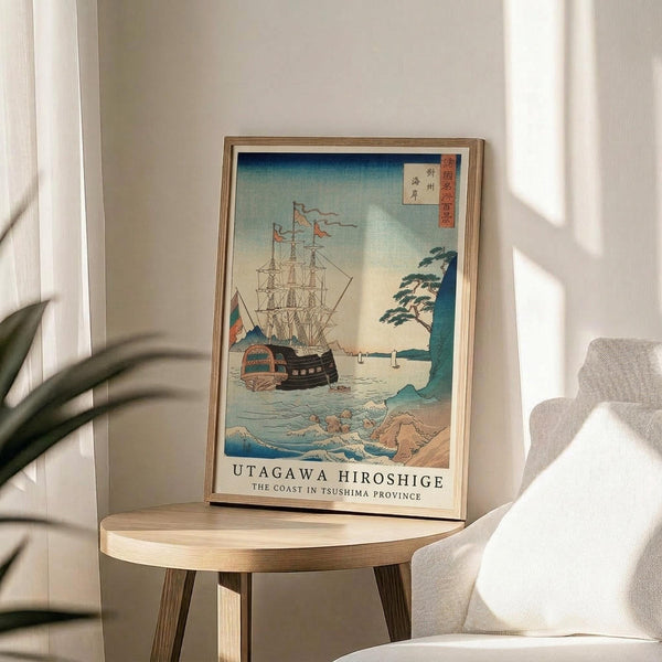 May include: Japanese woodblock print style poster in wooden frame displaying sailing ships on blue-green ocean waters with coastal landscape and traditional calligraphy. Artwork sits on round wooden side table next to beige upholstered chair, with plant leaves visible in corner and natural window light creating shadows on neutral wall.