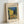 May include: Framed poster print of Van Gogh's Café Terrace at Night painting displayed against white wall. Shows yellow café building with outdoor seating under starry blue night sky, cobblestone street scene. Light wooden frame contains cream-colored mat with artwork title and 1888 date. Print features vibrant yellows, blues, and greens in Van Gogh's distinctive brushstroke style.