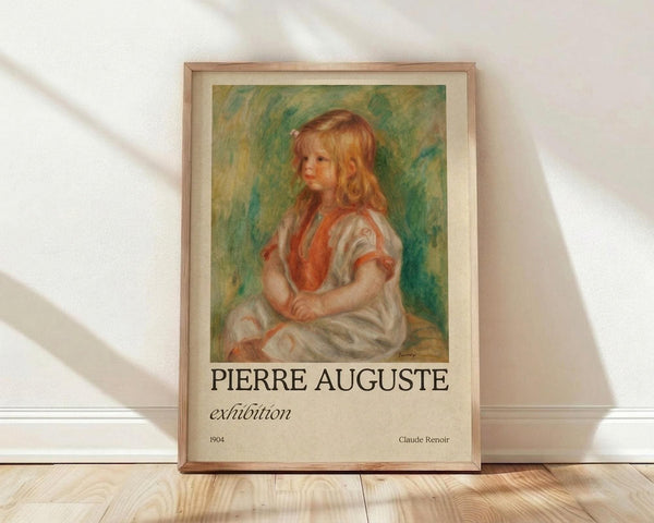 May include: Framed art print featuring a young girl with blonde curly hair wearing a white dress with red vest, painted in soft impressionist style with green and yellow background. The poster displays "PIERRE AUGUSTE exhibition" text below the artwork with "1904" and "Claude Renoir" attribution. Wooden frame rests against white wall on light wood floor with natural sunlight casting diagonal shadows across the scene.