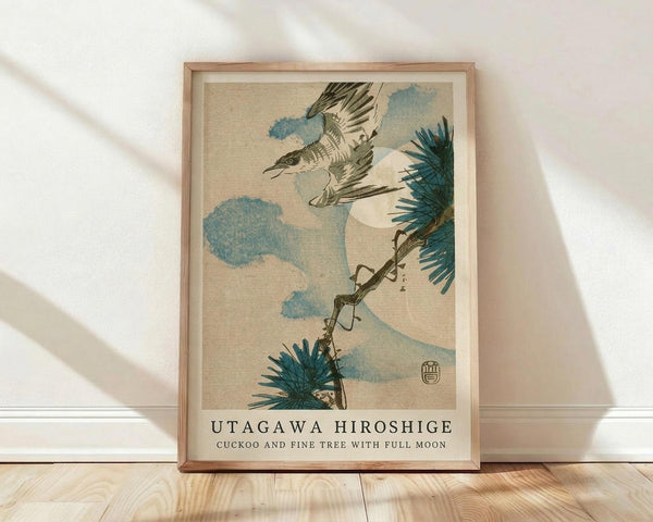 May include: Framed vintage Japanese woodblock print showing a cuckoo bird in flight among pine branches and blue clouds against a cream background. The artwork displays traditional ukiyo-e style with muted earth tones and delicate linework. Wooden frame sits on light wood flooring against white wall with natural sunlight casting shadows across the scene.