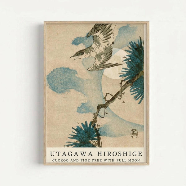 Japanese woodblock print featuring a cuckoo bird in flight with outstretched wings against a cloudy sky. The artwork shows pine branches with blue-green needles in the composition, rendered in traditional ukiyo-e style with muted earth tones and soft blue clouds. A circular moon or sun appears in the background. The print is displayed in a light wooden frame against a white wall, with the artist's signature seal visible in the lower right corner.