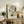 May include: Framed Japanese woodblock print featuring a flying bird with spread wings above pine branches and blue clouds against a beige background, displayed on a rustic wooden sideboard alongside fern plant, ceramic vase, books, and table lamp in a cozy living room setting with upholstered chair.