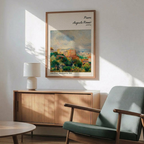 May include: Framed Renoir reproduction poster displayed above wooden credenza in minimalist living room with mid-century green armchair, white ceramic table lamp, and circular coffee table. Artwork shows impressionist landscape with buildings, lush green foliage, and cloudy sky in warm earth tones. Natural sunlight creates geometric shadows on white wall.