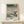 May include: Framed Japanese woodblock print featuring people with umbrellas crossing a snowy waterfront scene in traditional ukiyo-e style, displayed on light wood furniture with small wrapped gift, showing teal water, falling snow, and winter landscape with buildings and trees in muted colors