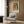 May include: Framed art print featuring a young girl with reddish-blonde hair in a white dress with coral accents, painted in impressionist style against green background. Text reads "Pierre Auguste exhibition" with "Claude Renoir" attribution. Displayed above a cream upholstered armchair with geometric patterned pillow in a modern room with wood paneling, brass floor lamp, and side table with open book.