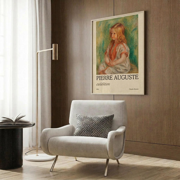 May include: Framed art print featuring a young girl with reddish-blonde hair in a white dress with coral accents, painted in impressionist style against green background. Text reads "Pierre Auguste exhibition" with "Claude Renoir" attribution. Displayed above a cream upholstered armchair with geometric patterned pillow in a modern room with wood paneling, brass floor lamp, and side table with open book.