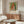 May include: Framed vintage art poster featuring Pierre-Auguste Renoir's portrait of a young girl with blonde hair wearing white and coral clothing against green background. Poster displayed above mid-century modern walnut credenza with brass hardware. Scene includes white curved lounge chair, round glass coffee table with wood base, and brass floor lamp in bright minimalist living room with white walls.