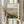 May include: Hands holding a framed print of a Renoir landscape painting showing colorful buildings and lush green vegetation from an elevated viewpoint, with dried pampas grass visible to the left, against white curtains and neutral background
