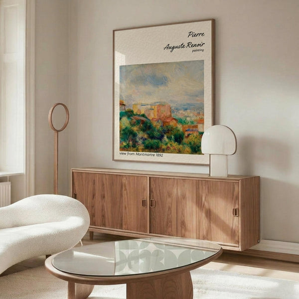 May include: Framed Renoir landscape poster hanging above wooden sideboard in minimalist living room with white curved chair, glass oval coffee table, and modern lamp. The vintage-style art print shows colorful buildings and greenery in impressionist painting style with cream matting and thin frame.