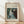 May include: Framed art print featuring Renoir's impressionist painting of a woman in a flowing white dress playing piano, displayed in light wood frame against white wall on wooden floor with soft natural lighting casting diagonal shadows across the scene.