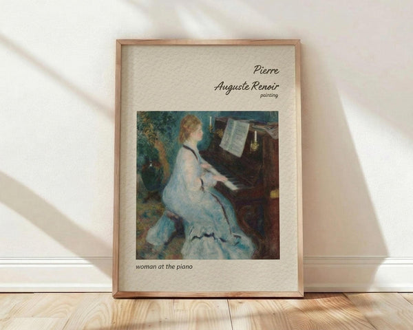 May include: Framed art print featuring Renoir's impressionist painting of a woman in a flowing white dress playing piano, displayed in light wood frame against white wall on wooden floor with soft natural lighting casting diagonal shadows across the scene.