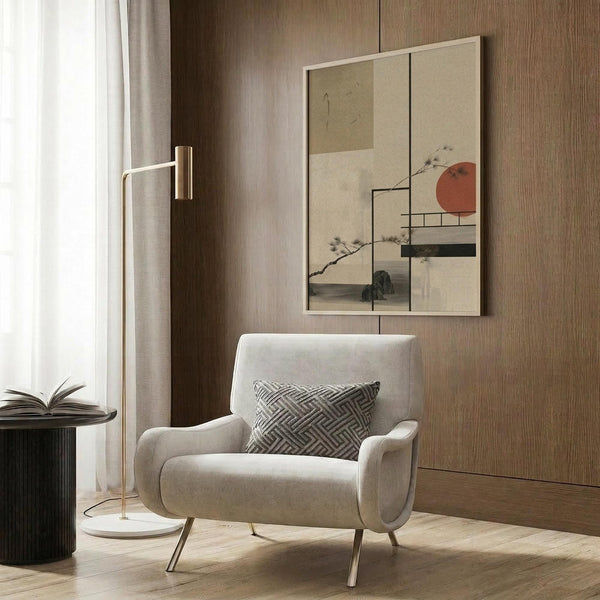 May include: Framed artwork displaying abstract geometric composition with rust-colored circle, black horizontal bars, and delicate branch illustrations on neutral background. Modern beige armchair with geometric patterned pillow sits beside brass floor lamp in contemporary room with wood-paneled walls and soft natural lighting from window.