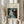 May include: hands holding a framed art print of Renoir's impressionist painting showing a woman in a white dress playing piano, with dried pampas grass stems, against white curtained background in natural lighting