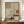 May include: Framed artwork with Japanese-inspired design featuring geometric sections in beige and cream tones, black pine branches, terracotta sun, and dark green landscape elements. Displayed on wooden sideboard beside white ceramic vase and stacked books in elegant room with cream walls and white trim molding.