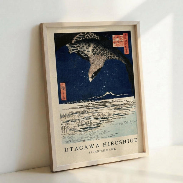 May include: Framed reproduction of Japanese woodblock print showing large hawk with detailed feathers flying against deep blue starry night sky above snowy landscape with mountains and small village. Traditional red text cartouches visible in corners. Print displayed in light wooden frame leaning against white wall.