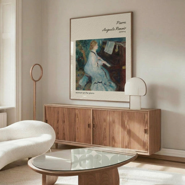 May include: Framed art print of Renoir's "Woman at the Piano" showing a woman in a white dress playing piano, displayed above a wooden sideboard with sliding doors in a modern living room with cream walls, white curved chair, glass oval coffee table, and brass floor lamp with circular mirror detail.
