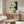 May include: Abstract geometric poster with cream, black, and olive green curved shapes, fine line details, and small black circles mounted above a walnut wood credenza in a modern living room with white curved chair, glass oval coffee table, and warm natural lighting.