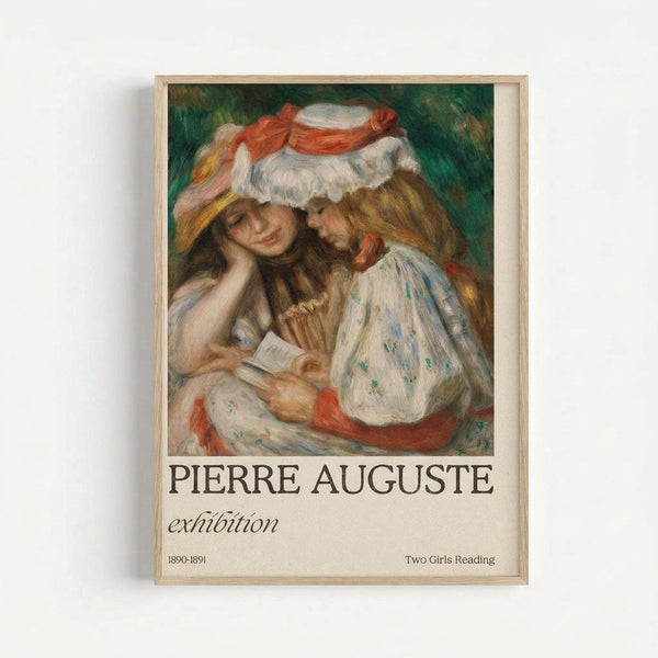 Framed exhibition poster featuring a soft impressionist painting of two young women in white dresses with floral patterns reading together. One wears a wide-brimmed hat with red ribbon and white trim. The artwork shows warm peachy skin tones against a green background. Text below reads "PIERRE AUGUSTE exhibition" with "1890-1891" and "Two Girls Reading" in smaller print. Natural wood frame against white wall.