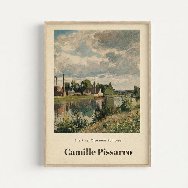 May include: Framed art print of an impressionist landscape painting showing a river scene with industrial buildings, smokestacks, and boats along the waterway. The artwork features soft brushstrokes in muted greens, blues, and earth tones depicting countryside with cloudy skies. Below the image is text reading "The River Oise near Pontoise" and "Camille Pissarro" in black lettering on cream-colored paper, displayed in a light wood frame against a white wall.